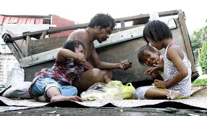 Father with 3 chldren eating food on the street in a very impoverished setting