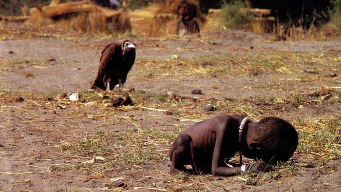 Very weak and  thin boy  touching  the  ground  with  his  forefront while a vulture is  by his  side waiting