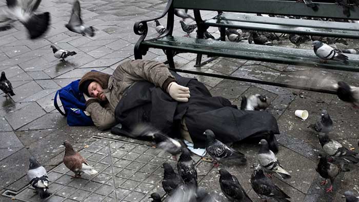 Hombre durmiendo en la calle mientras las palomas están a su alrededor