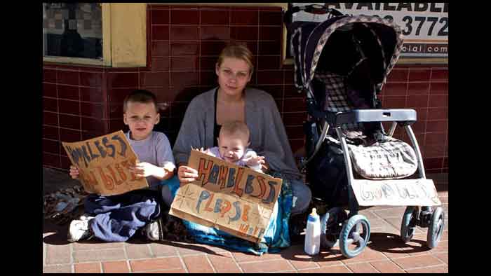 Mamá joven con sus 2 pequeños hijos sosteniendo 2 avisos: ‘Sin hogar. Dios te bendiga’ , ‘Sin hogar. Por favor ayuda'