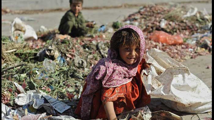 2  kids searching  in  garbage dump, smiling while looking  at  the  camera